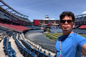 A student with a blue shirt and sunglasses photographs himself in the stands of the World Cup stadium.