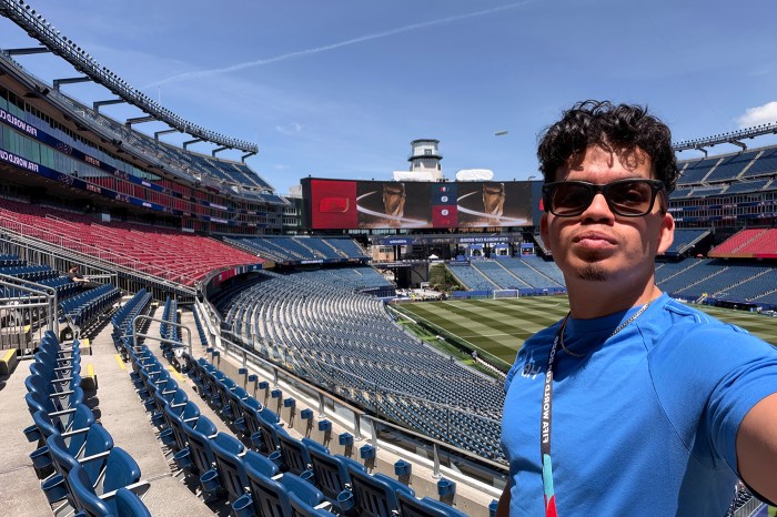 A student with a blue shirt and sunglasses photographs himself in the stands of the World Cup stadium.