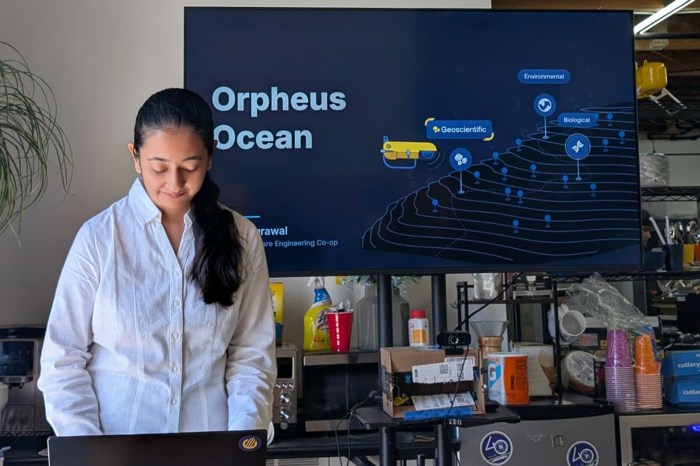 Shalini Agrawal presents on a laptop in front of a screen displaying the Orpheus Ocean project slide.
