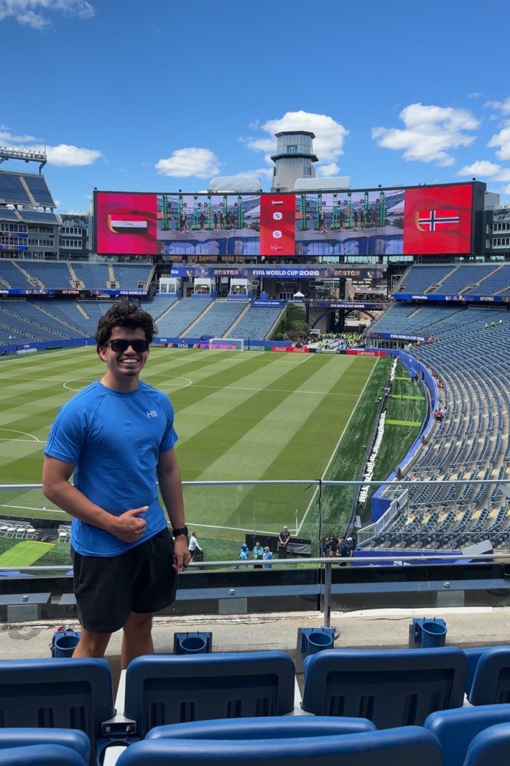 A student wearing a blue T-shirt and sunglasses is seen in the stands of the World Cup stadium.