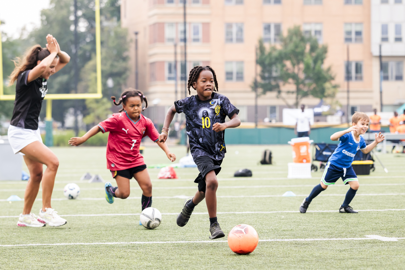 Young children play soccer on a field, chasing after the ball.