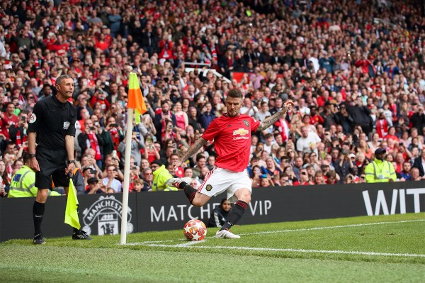 David Beckham lines up a corner kick in a crowded stadium, with a referee and assistant referee looking on near the corner flag.