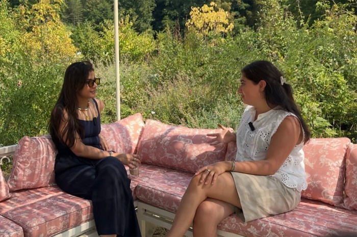 Two people sit on a cushioned seat surrounded by foliage.