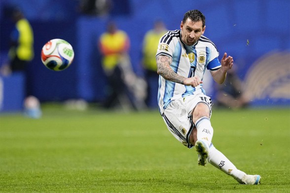 Lionel Messi mid-kick while a ball flies through the air in front of him.