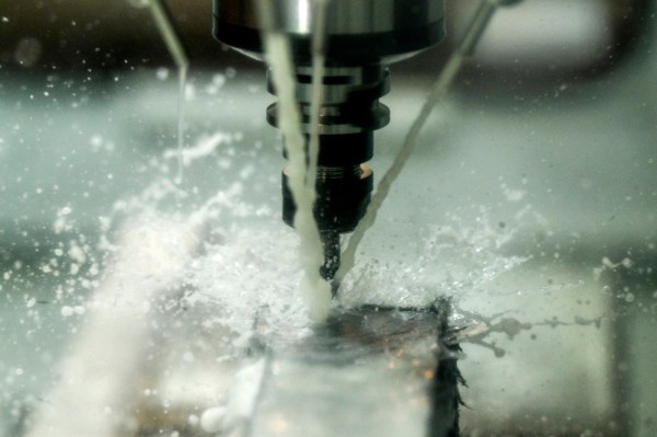 A CNC machine drilling into metal, with coolant fluid spraying around the cutting tool.
