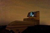 Vera C. Rubin Observatory's dome under a star-filled night sky at Cerro Pachón, Chile, with its telescope shutter open and interior lit.