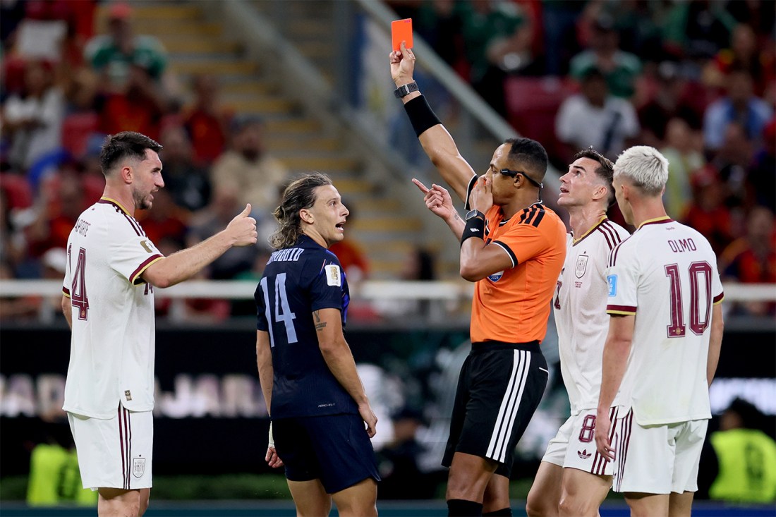 Referee Ismail Elfath points while showing a red card, surrounded by Uruguay and Spain players reacting.