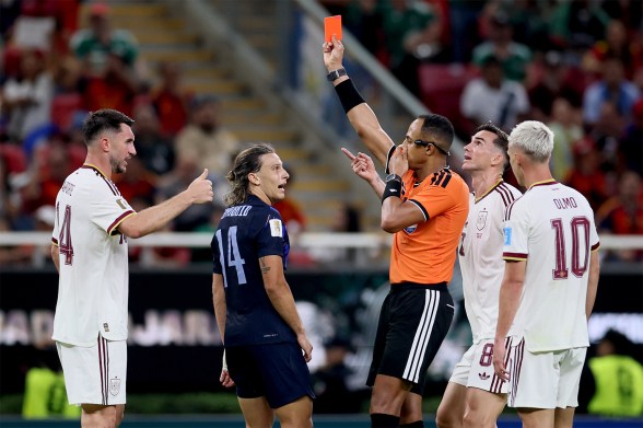 Referee Ismail Elfath points while showing a red card, surrounded by Uruguay and Spain players reacting.
