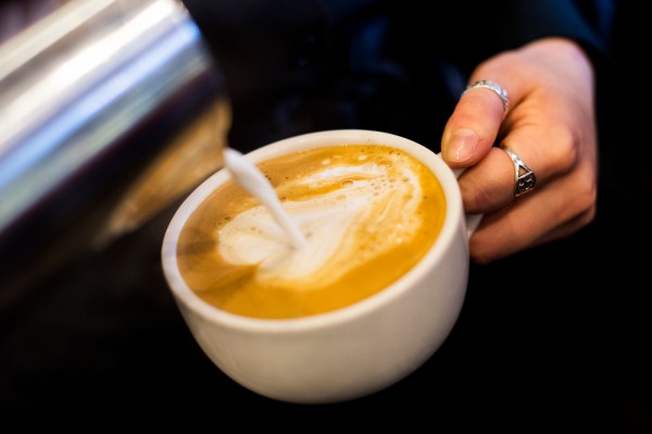 A hand pours milk into a cup of coffee, creating a swirl pattern on the surface.