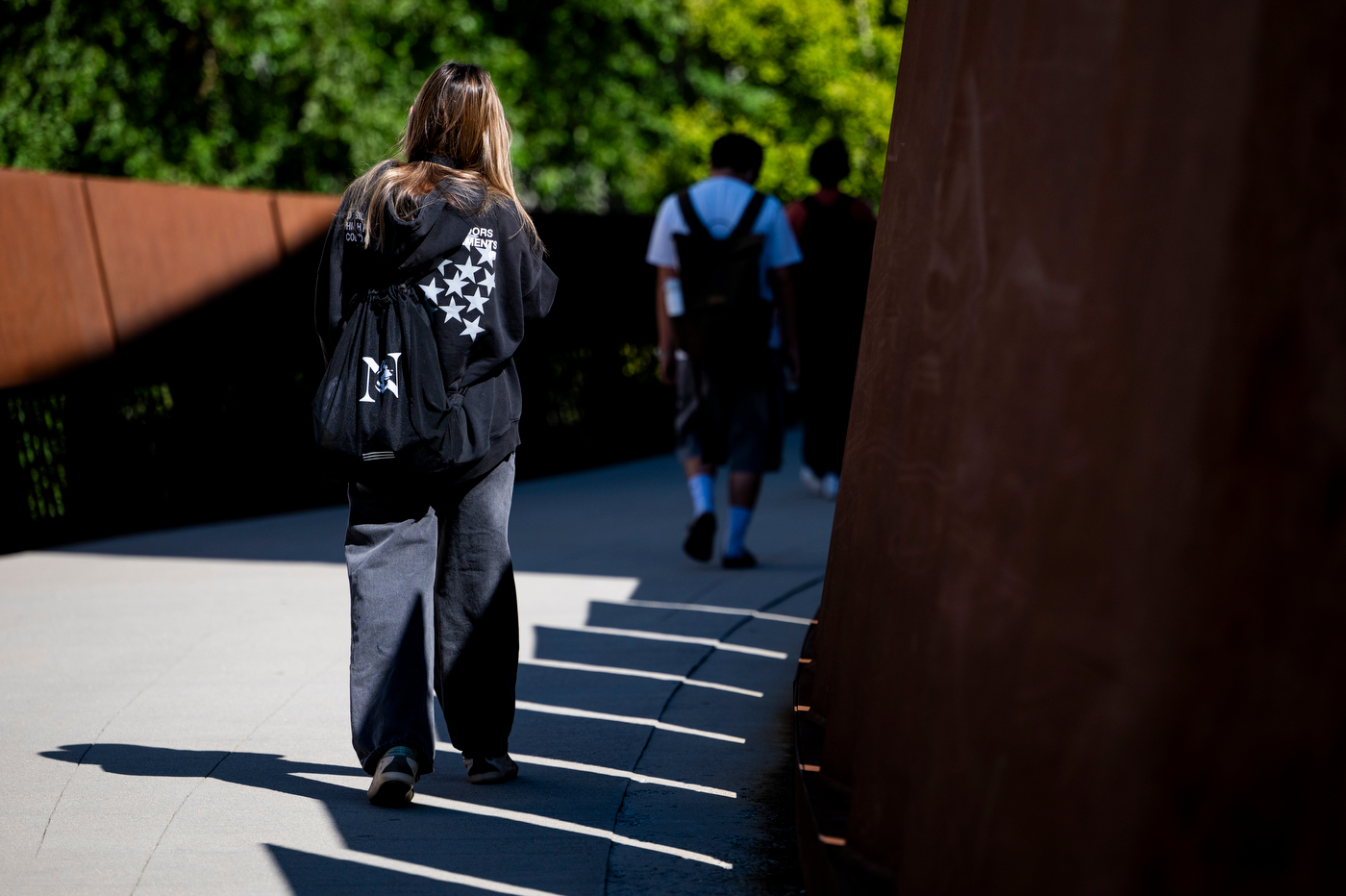 Students in backpacks walk across the pedestrian bridge.