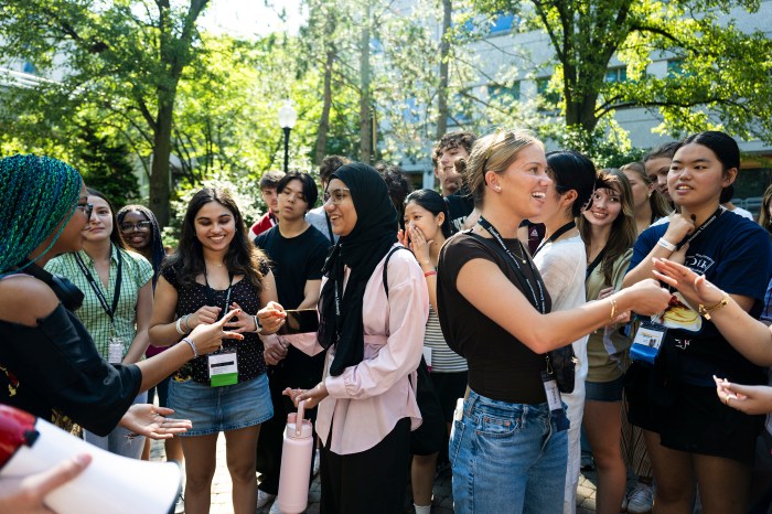 crowd of incoming freshmen laugh and play rock-paper-scissors together outdoors.