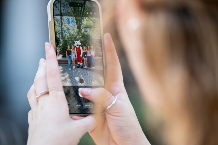 A student photographs Paws the mascot posing with orientation leaders on a smartphone.