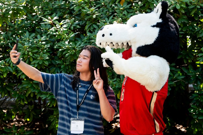 A student takes a selfie with Paws the husky mascot.
