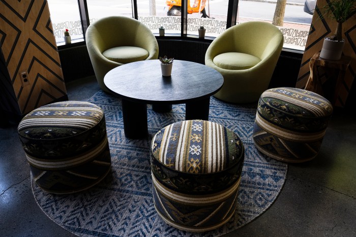 Green armchairs and patterned pouf seating around a round table inside Nuba by Nubian Markets.