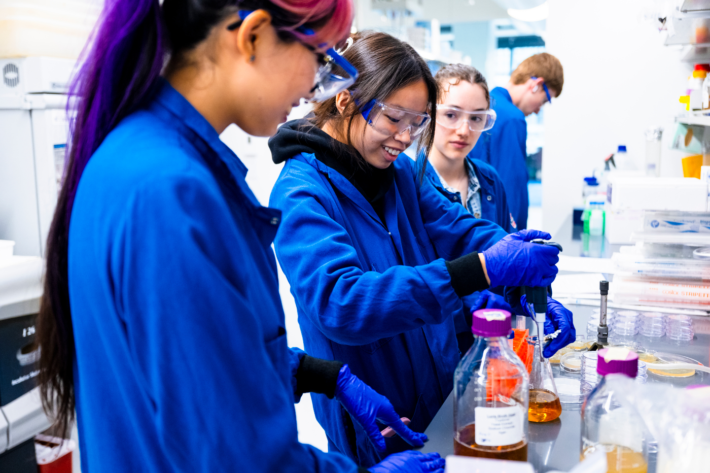 Amy Pham and classmates, wearing lab coats and safety goggles, work with beakers of chemicals.