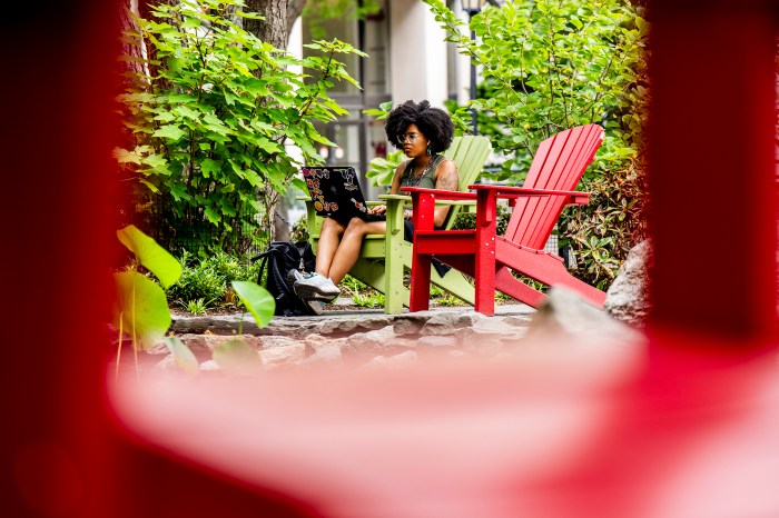 Student studies on a laptop in a red Adirondack chair beside the koi pond near Curry Student Center.