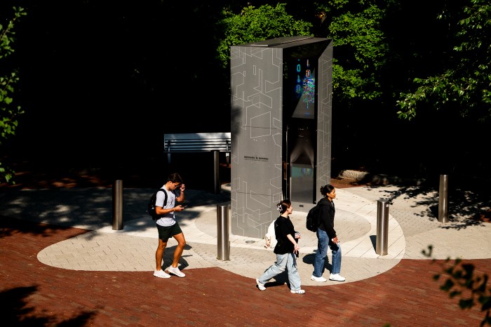 A person walks past a stone monument and screen display on campus.