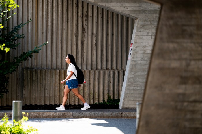 A student with a black black pack walks through campus. 