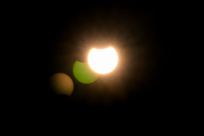 Partial solar eclipse visible in the night sky, with the moon covering only part of the sun.