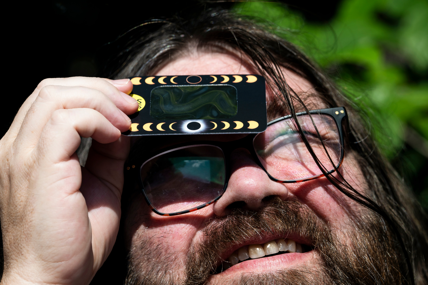 Close-up of a person holding eclipse glasses up to view the partial solar eclipse.