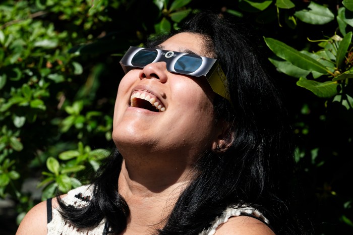 A staff member smiles while looking up through eclipse glasses