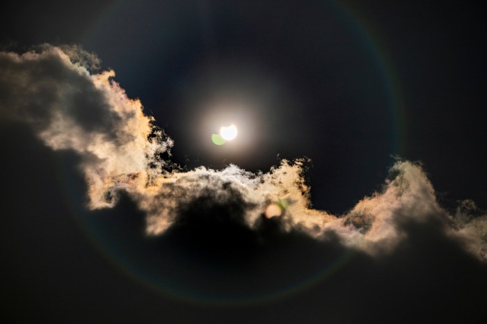 Partial solar eclipse visible through wispy clouds.