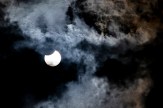 A partial solar eclipse visible through thick cloud cover, the moon's silhouette taking a bite out of the sun's disk.