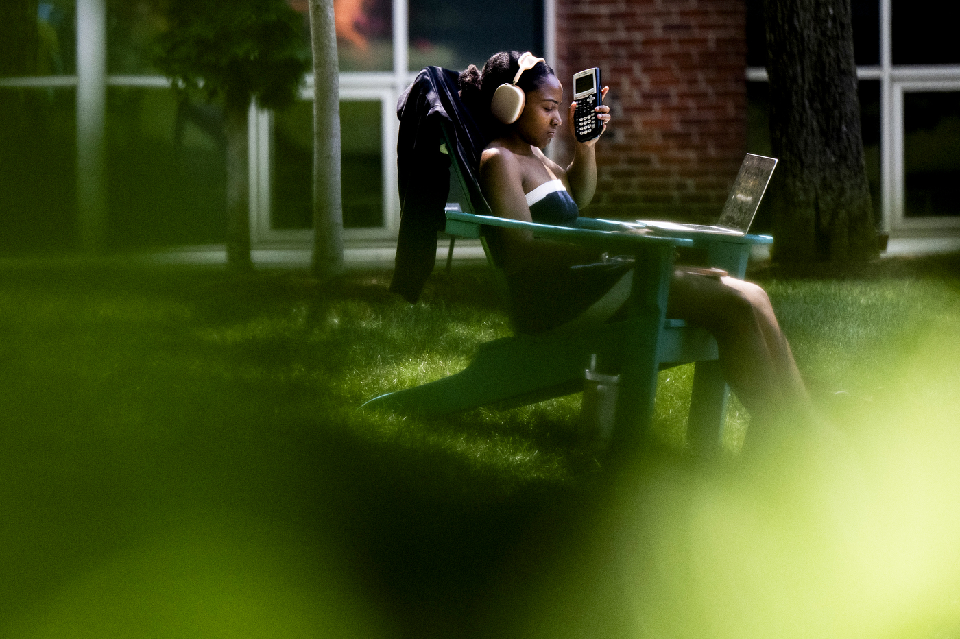 A person sits on an adirondack chair while doing school work.