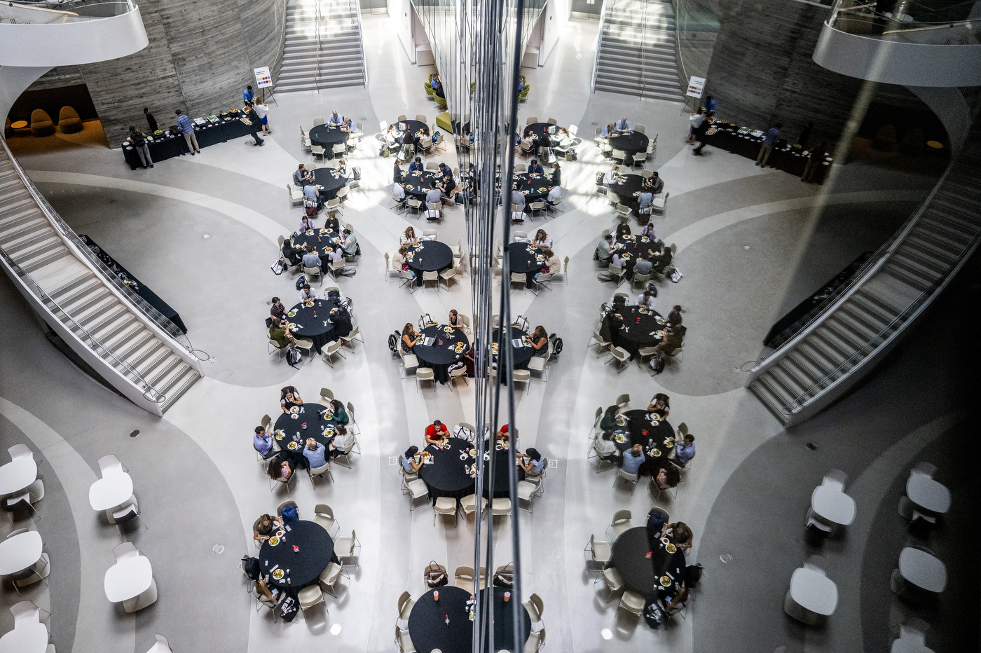 Aerial view of people seated at round tables in the open atrium of a Northeastern building, with curved staircases on either side.