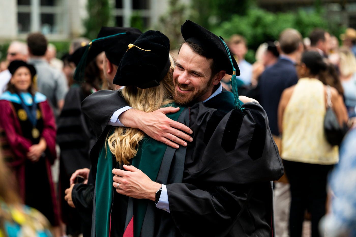 Graduates in caps and gowns embrace in a group hug outdoors after the Bouvé College Physical Therapy Graduation.