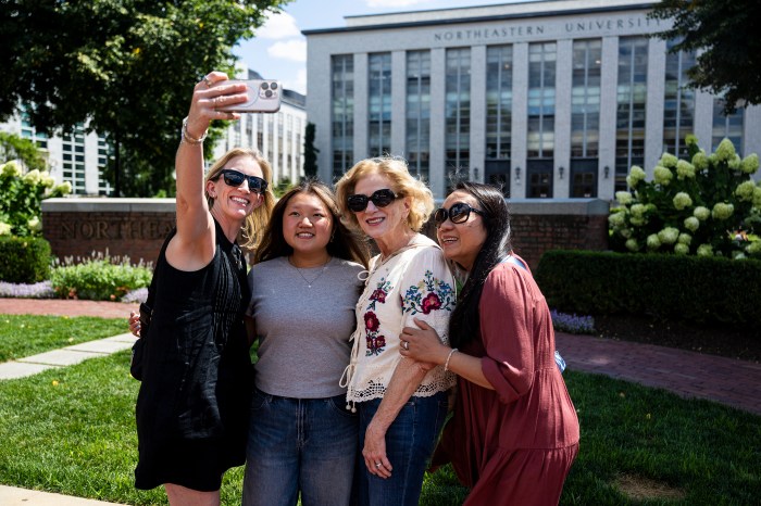 An incoming student takes a selfie with three family members in Krentzman Quad, with Northeastern's campus buildings in the background.
