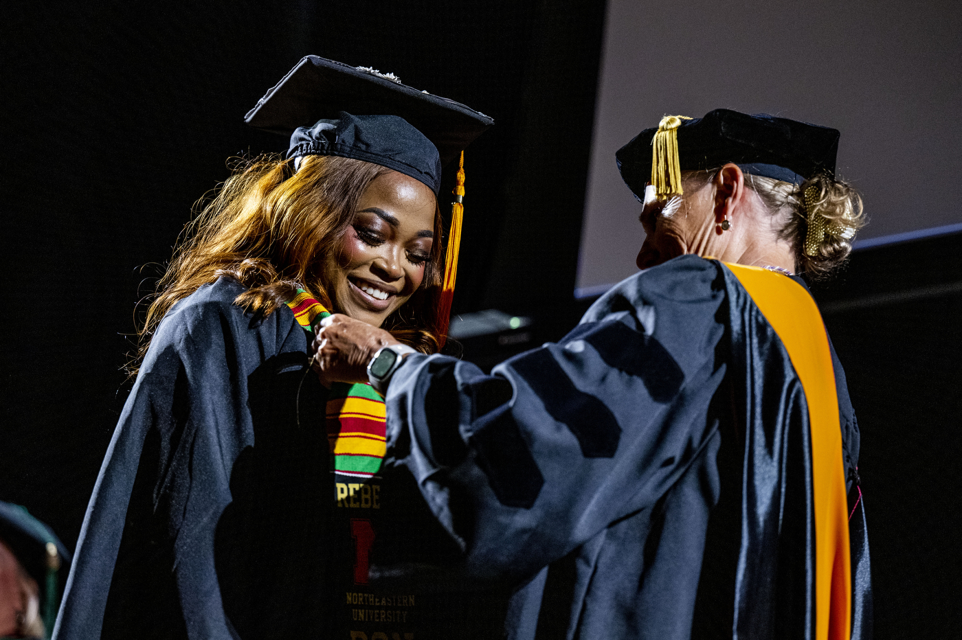 Nursing graduate smiles while receiving her pin from a faculty member on stage during the ceremony.