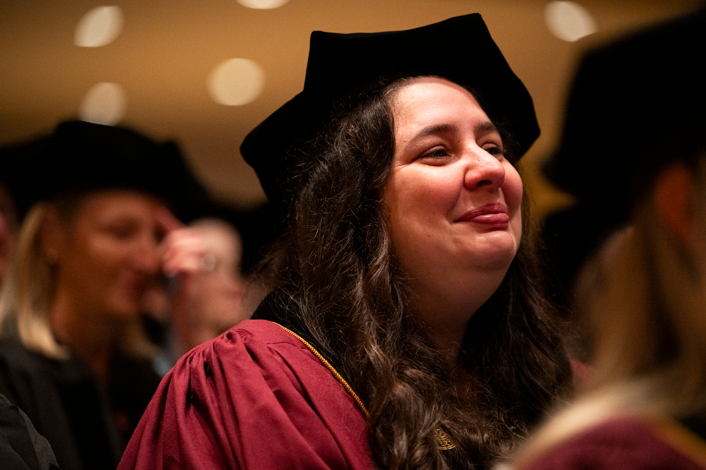 Close-up of a graduate in doctoral cap and gown smiling with emotion during the ceremony.