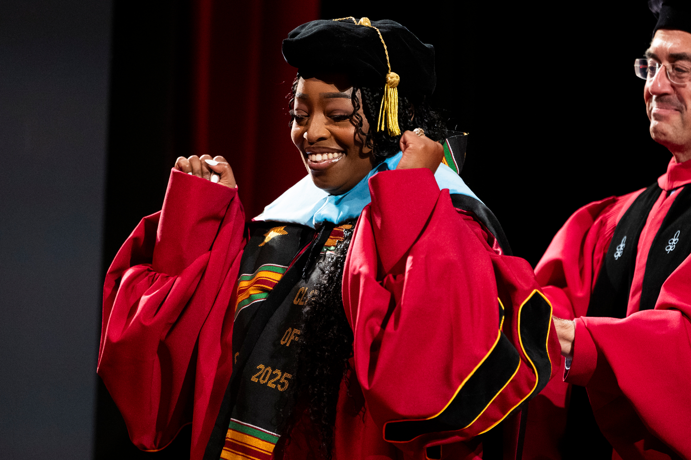Graduate smiles while faculty members help adjust her doctoral robe during the College of Professional Studies Doctoral Commencement Ceremony.
