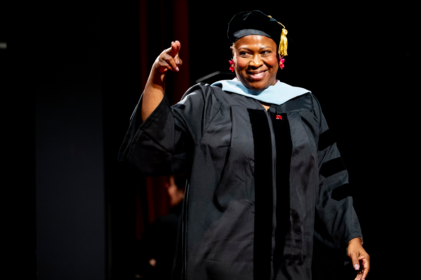 Doctoral graduate smiles and points while walking across the stage during the College of Professional Studies Commencement Ceremony.