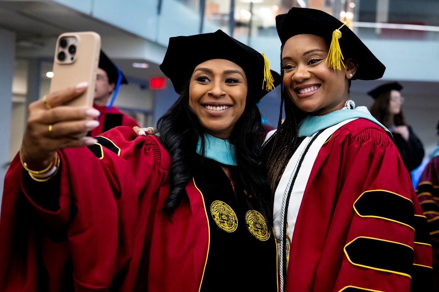 Two graduates in doctoral regalia smile while taking a selfie together at the College of Professional Studies Doctoral Commencement Ceremony.