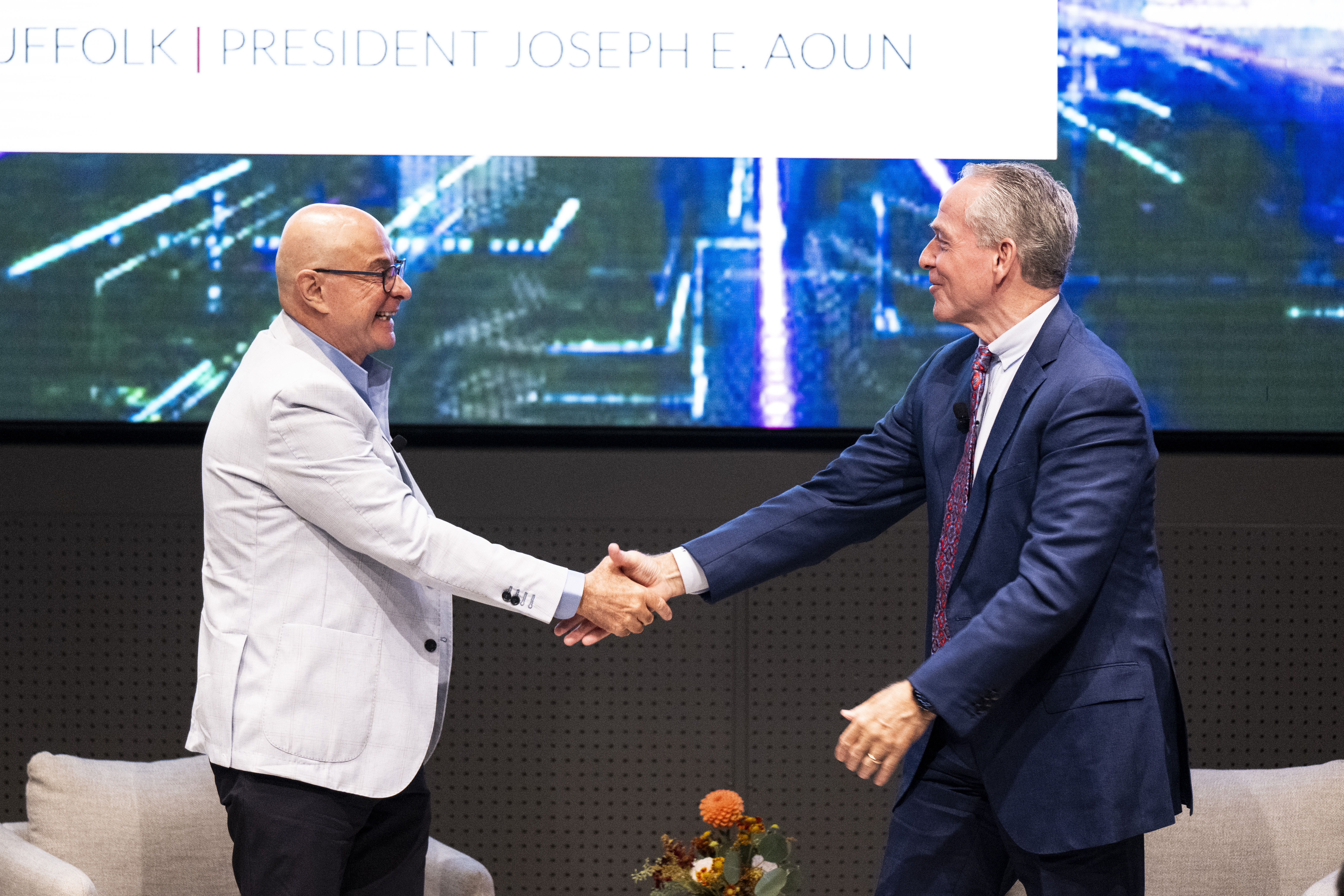 John F. Fish, CEO of Suffolk Construction, and Northeastern President Joseph E. Aoun shaking hands on stage.