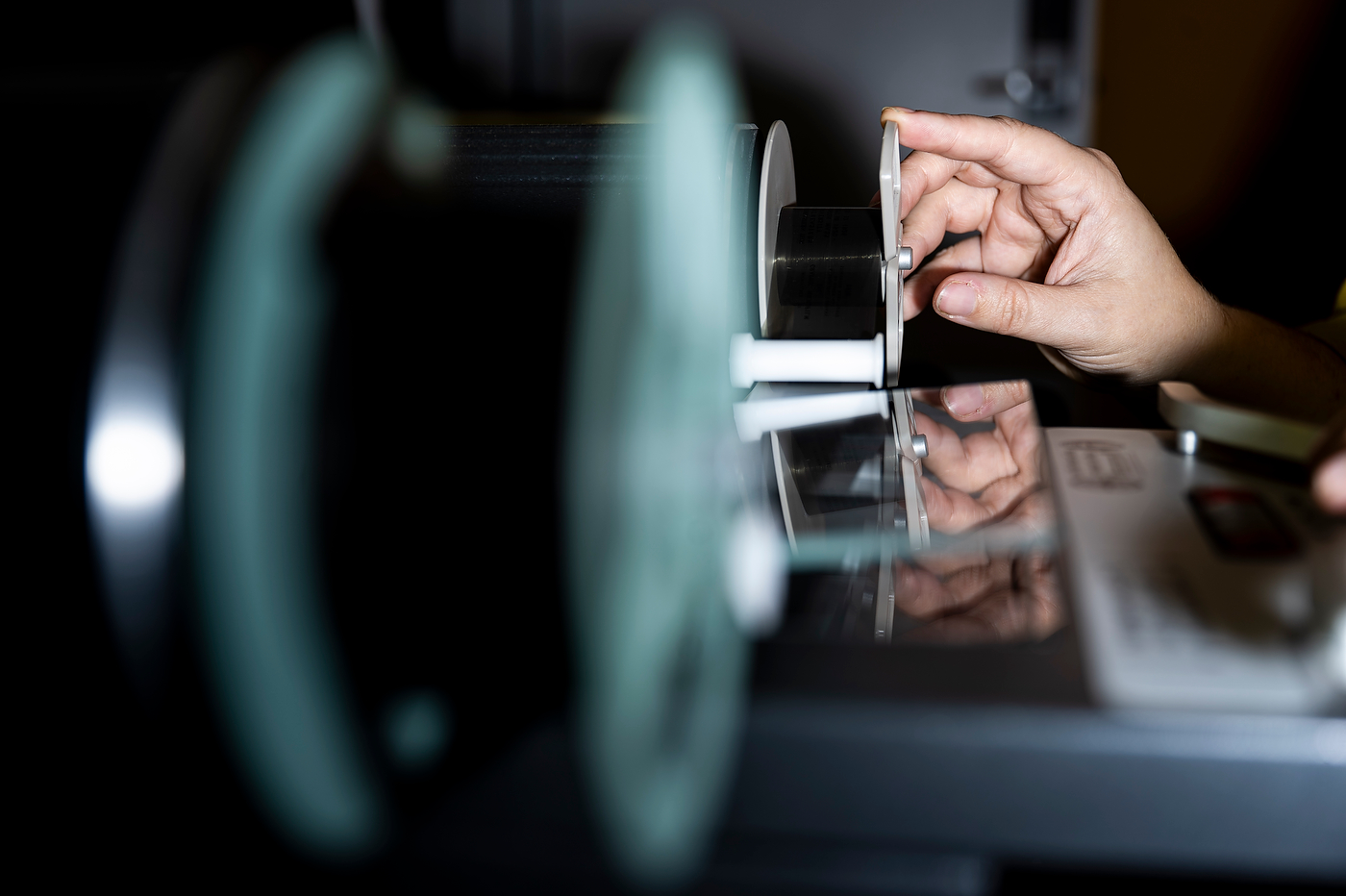 Close-up of hands threading film through the spools of a microfilm reader.