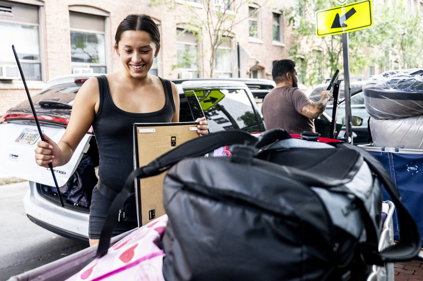 A woman stacks her belongings into a move-in cart next to cars parked along the street.