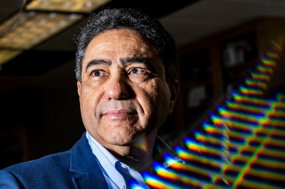 Ahmed Busnaina looking off-camera, with a wall behind him lit by scattered rainbow-colored light reflections.