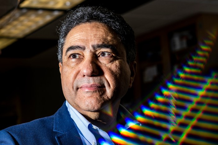 Ahmed Busnaina looking off-camera, with a wall behind him lit by scattered rainbow-colored light reflections.