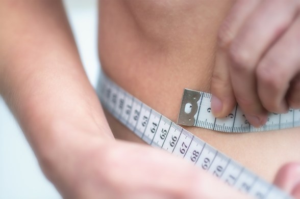 Close-up of a person measuring their waist with a tape measure.