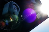 A Flock Safety surveillance camera mounted on a pole, shot from below with bright sun flare in the frame.