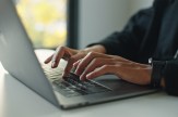 Close-up of a person's hands typing on a laptop keyboard, face out of frame.
