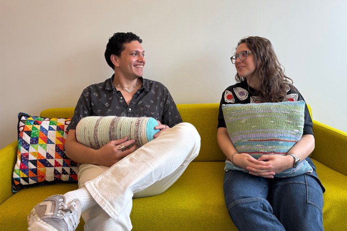 Two people holding crafted data textiles smile while sitting on a couch.