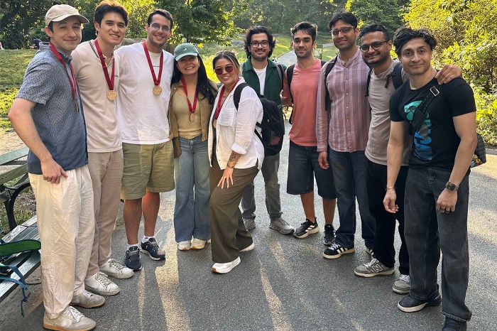 Group of ten colleagues posing together outdoors on a paved path, some wearing medals around their necks.