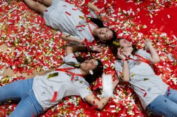 Northeastern students lying on the ground at Convocation surrounded by confetti, shot from overhead.