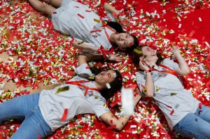 Northeastern students lying on the ground at Convocation surrounded by confetti, shot from overhead.
