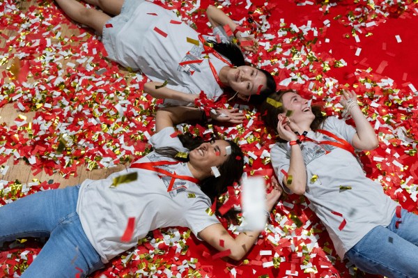 Northeastern students lying on the ground at Convocation surrounded by confetti, shot from overhead.