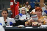 Workers wearing blue gloves sit at tables examining ballot envelopes and papers.